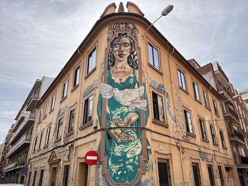 woman in a green dress with a white dove in front on the corner of the building