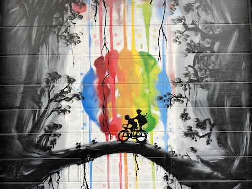 black and white scene with two kids on a bike with a rainbow circle in the background