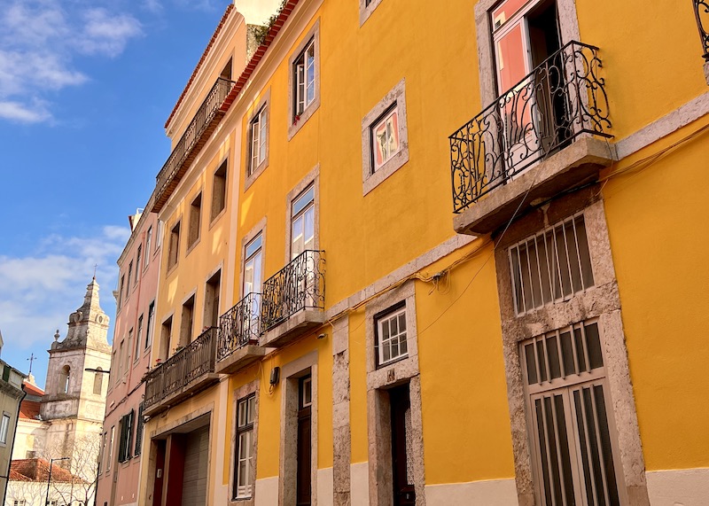 yellow apartment building in Lisbon with a church at the end. Golden Visa How to Live Abroad