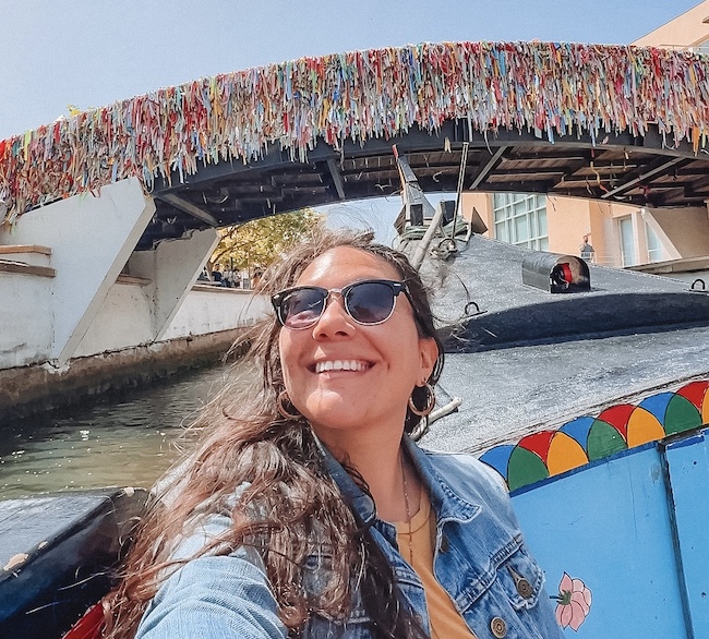 brunette with sunglasses sitting in a moliceiro under a bridge with colorful tassels. beautiful cities in portugal