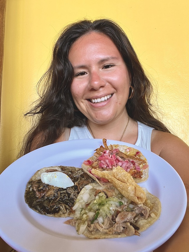 brunette holding a plate with three different tacos - Mexican Caribbean Coast