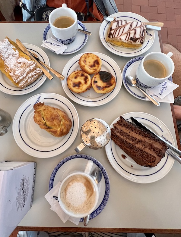 multiple desserts including chocolate cake, mil folhas, pasteis de Belem and three coffees with milk