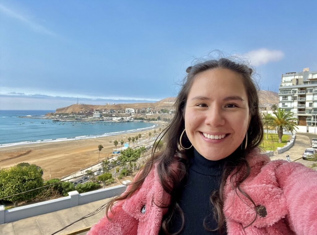 smiling brunette in a black shirt and pink jacket standing in front of a view of Lima